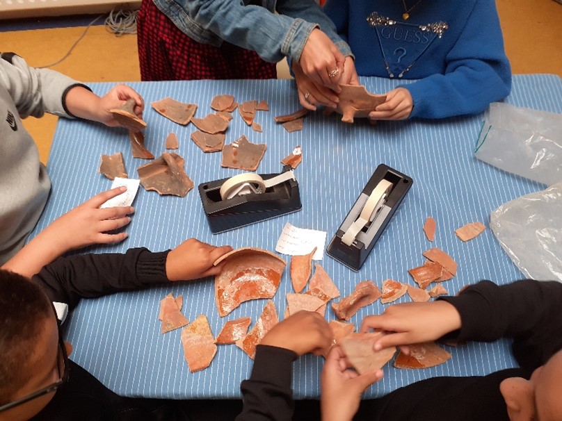 Kinderen herstellen gebroken kunstvoorwerpen aan tafel.